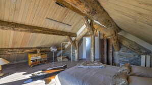 A rustic bedroom with exposed wooden beams, a stone wall, and a bed with a fur throw. - 5-star log cabin with SPA (Erckartswiller)