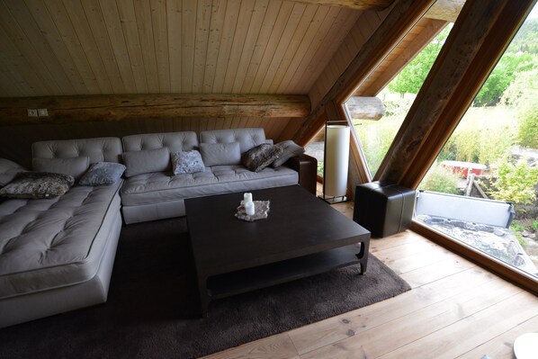 A modern loft-style living room with a sectional sofa, a coffee table, and a large window offering a view of the outdoors.