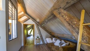 A loft bedroom with exposed wooden beams, a wooden floor, a sofa with cushions, and a ladder. - 5-star log cabin with SPA (Erckartswiller)