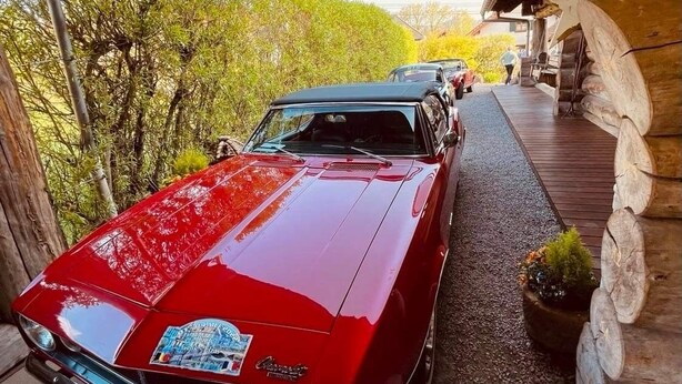 A red classic car parked under a wooden structure with a view of trees and a clear sky. - 5-star log cabin with SPA (Erckartswiller)