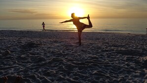 A beach with a person performing a yoga pose, another person walking, and the sun setting in the background. - Perfect recipe for relaxing, heated pool, walk to beach, bikes, stunning sunsets (Naples)