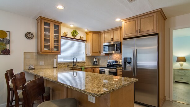 A kitchen with granite countertops, wooden cabinets, stainless steel appliances, and a breakfast bar. - Perfect recipe for relaxing, heated pool, walk to beach, bikes, stunning sunsets (Naples)