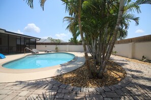 Una piscina circondata da palme e un patio con un vialetto in mattoni.