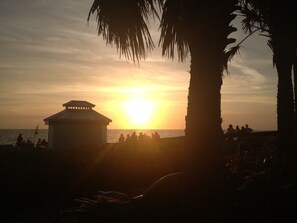 Scena di spiaggia con un edificio e palme al tramonto.