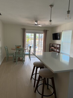 Una cocina con una isla central, taburetes de bar, un ventilador de techo y un televisor en la pared.