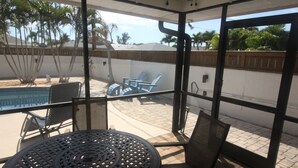 A covered patio with a pool, chairs, and a table. - Perfect recipe for relaxing, heated pool, walk to beach, bikes, stunning sunsets (Naples)
