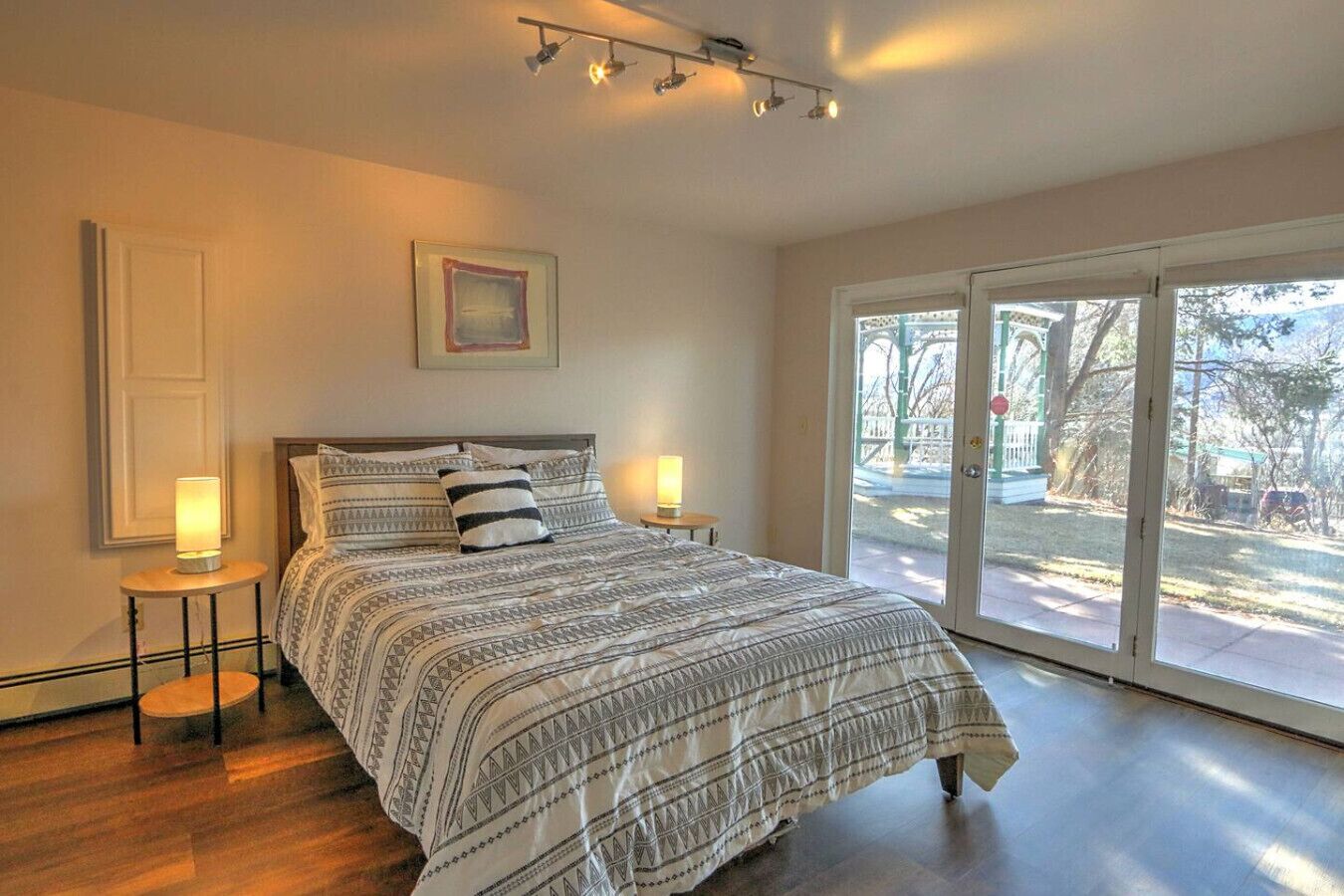 Una camera da letto con un letto grande, due comodini con lampade, un quadro appeso al muro e una porta scorrevole in vetro che dà su uno spazio esterno.