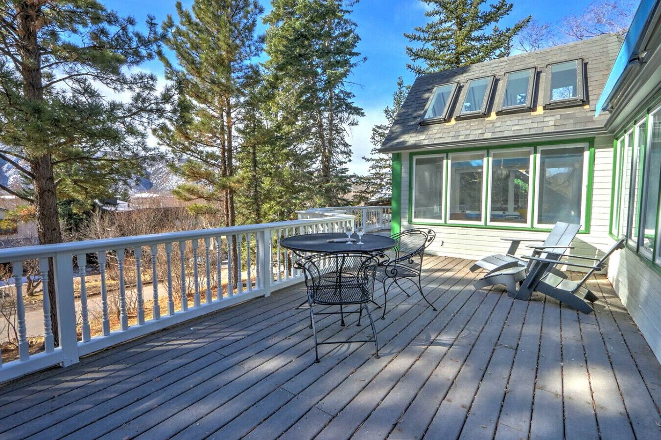 A wooden deck with a table and chairs, surrounded by trees and a house with large windows.