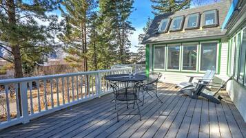 A wooden deck with a table and chairs, surrounded by trees and a house with large windows.