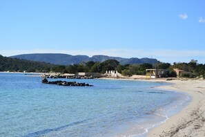 A beach with clear blue water, rocky outcrops, and a few buildings in the background. - VILLA SAN CIPRIANU - FEET IN THE WATER - BEACH ON FOOT (Saint-Cyprien Lecci)