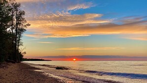 A beach with a sunset, trees, and a calm sea.