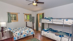 A bedroom with a bed, a desk, a dresser, a bunk bed, and a ceiling fan.