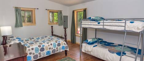 Un dormitorio con cama, escritorio, cómoda, literas y ventilador de techo.