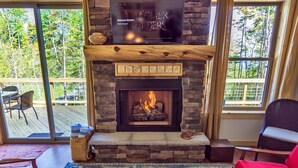 A fireplace with a TV above it, a red chair, and a wooden table with magazines.