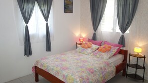 A bedroom with a wooden bed, floral bedding, two bedside lamps, and grey curtains. - Holiday rental "AUTHENTICITY and CONVIVIALITY" in DESHAIES GUADELOUPE (Deshaies)