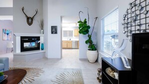 A modern living room with a fireplace, a large potted plant, and a wall-mounted mirror. - Desert Pool Oasis located in the heart of Las Cruces (Las Cruces)