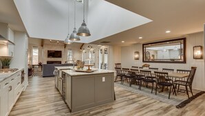 A spacious kitchen with a central island, pendant lighting, and a large dining area with wooden chairs and a table.