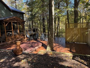 A wooden deck with Adirondack chairs, a large vase, and a covered seating area with a view of the forest. - Blue Ridge Pkway:Chef kitchen,Fenced YardPlayground,Hottub,5bdrms, 4public rooms (Boone)