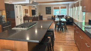 A modern kitchen with a large island, wooden cabinets, and a dining area with a view of the outdoors. - Blue Ridge Pkway:Chef kitchen,Fenced YardPlayground,Hottub,5bdrms, 4public rooms (Boone)