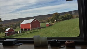 Une vue depuis une fenêtre donnant sur un paysage rural, avec des granges et des champs verdoyants.