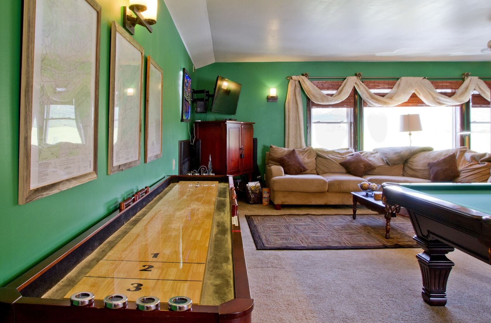 Een biljarttafel, een bank en een televisie in een kamer met groene wanden.