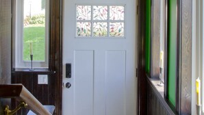 Un couloir avec un mur vert, une porte blanche ornée de vitraux et un luminaire suspendu.