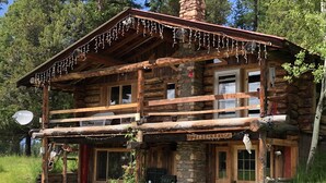 Une cabane rustique en rondins de bois, dotée d’un balcon, d’une cheminée en pierre et d’une enseigne indiquant « LAZIE BEAN RANCH ».