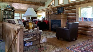 L’intérieur d’un chalet confortable, avec des murs en rondins de bois, une cheminée, des étagères à livres, une table basse et un coin salon accueillant.