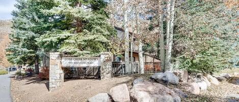Una entrada cerrada a Gore Creek Meadows, con un letrero de piedra, una valla de madera y un gran árbol de hoja perenne.