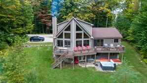 A two-story cabin with a deck, a hot tub, and a car parked in the driveway. - The Ridge Chalet, an A-Frame Killington Home (Killington)