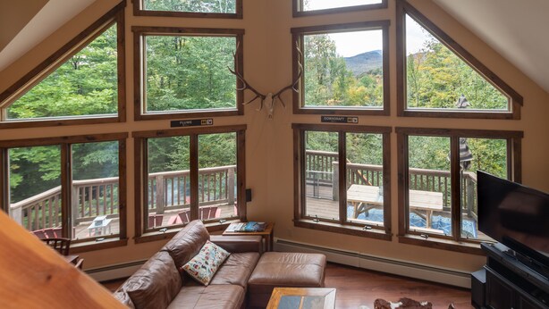 A spacious living room with a large window overlooking a deck and forest. - The Ridge Chalet, an A-Frame Killington Home (Killington)
