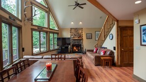 A spacious living room with a fireplace, a dining area, and a staircase leading to another level. - The Ridge Chalet, an A-Frame Killington Home (Killington)