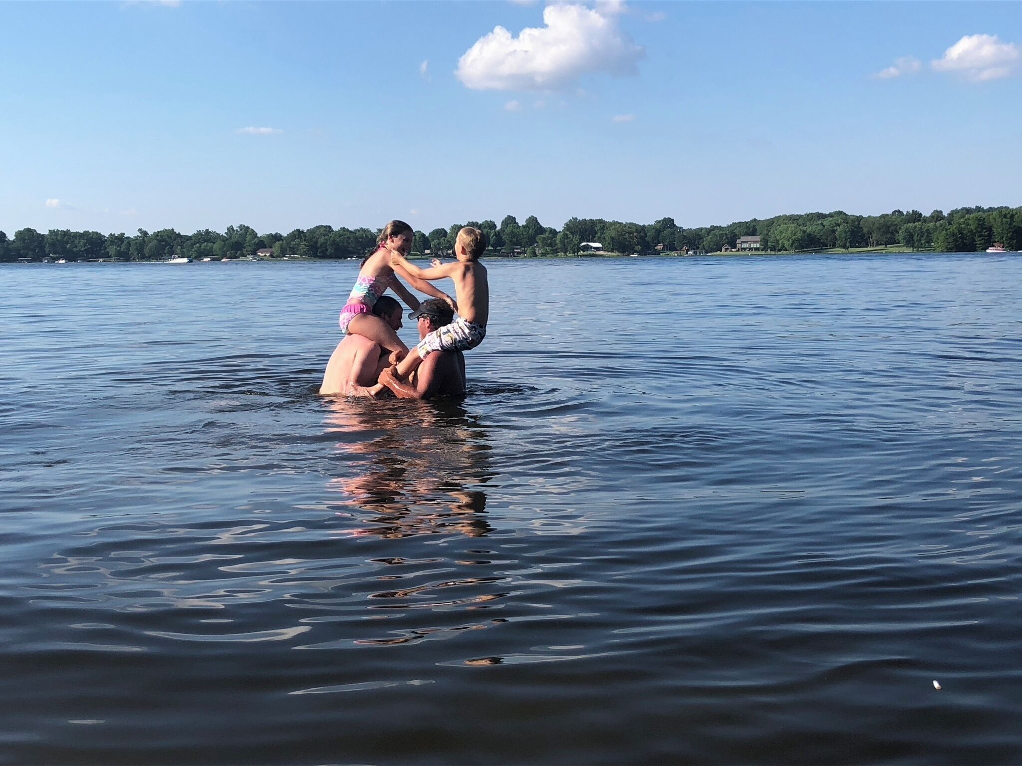 A group of people in a body of water with a distant shoreline and trees.