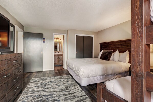 A bedroom with a large bed, wooden headboard, a dresser, and a bathroom visible through an open door. - Ski In Ski Out 2 Bed 3 bath, 1100sqft. Vaulted ceiling sleeps 10 in Ctr Village (Frisco)