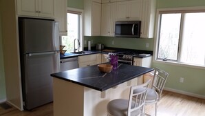 A kitchen with white cabinets, a stainless steel refrigerator, a microwave, and a wooden island with two chairs. - Beautiful, Remodeled Cottage in the Heart of Afton (Afton)