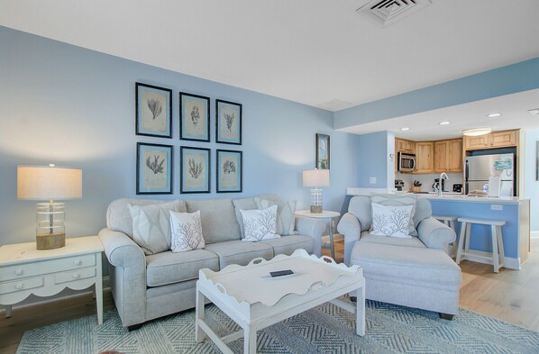 A living room with a sofa, two side tables, a coffee table, and framed botanical prints on the wall.