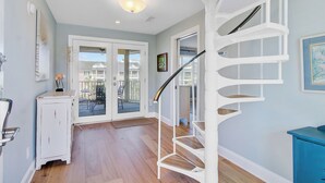 Un escalier en colimaçon dans un couloir, avec un plancher en bois, une porte blanche et une vue sur l’extérieur.