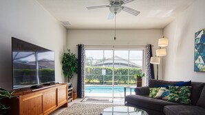 A living room with a flat-screen TV, a sofa, a coffee table, and a view of a swimming pool. - Windsor Palms Villa w/South Facing Private Pool & Hot Tub Close to Disney & Golf (Kissimmee)
