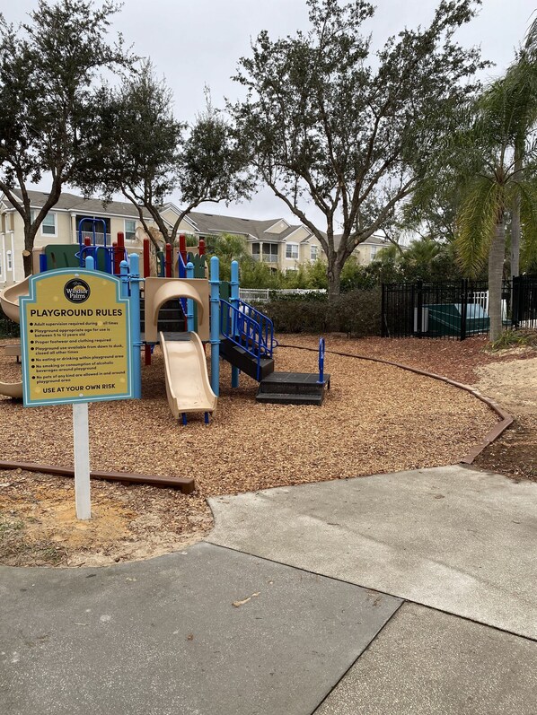 A playground with a slide and climbing structures, surrounded by trees and a fence. - Windsor Palms Villa w/South Facing Private Pool & Hot Tub Close to Disney & Golf (Kissimmee)