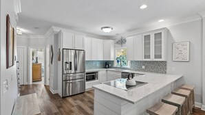 A modern kitchen with white cabinetry, stainless steel appliances, and a marble island with stools. - Award-Winning Resort Amenities | Grand Pavilion 10 (Isle of Palms)