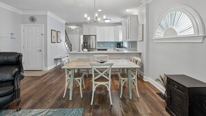 A modern kitchen with white cabinetry, a dining table with chairs, a black leather sofa, and a fireplace. - Award-Winning Resort Amenities | Grand Pavilion 10 (Isle of Palms)
