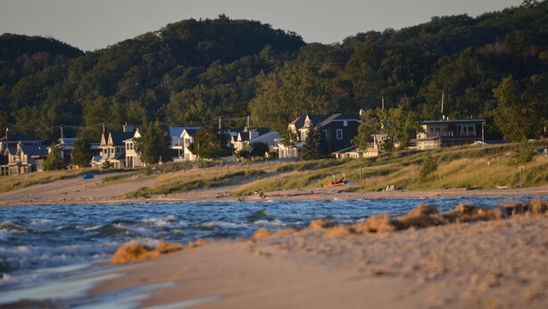Un pueblo costero con casas a lo largo de la playa y una colina boscosa al fondo.