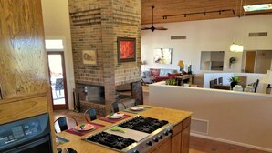 A kitchen with a brick fireplace, a gas stove, and a dining area with chairs and a table. - Rancho Venado Tucson, One of a kind, spiritual desert oasis in NE Tucson (Tucson)