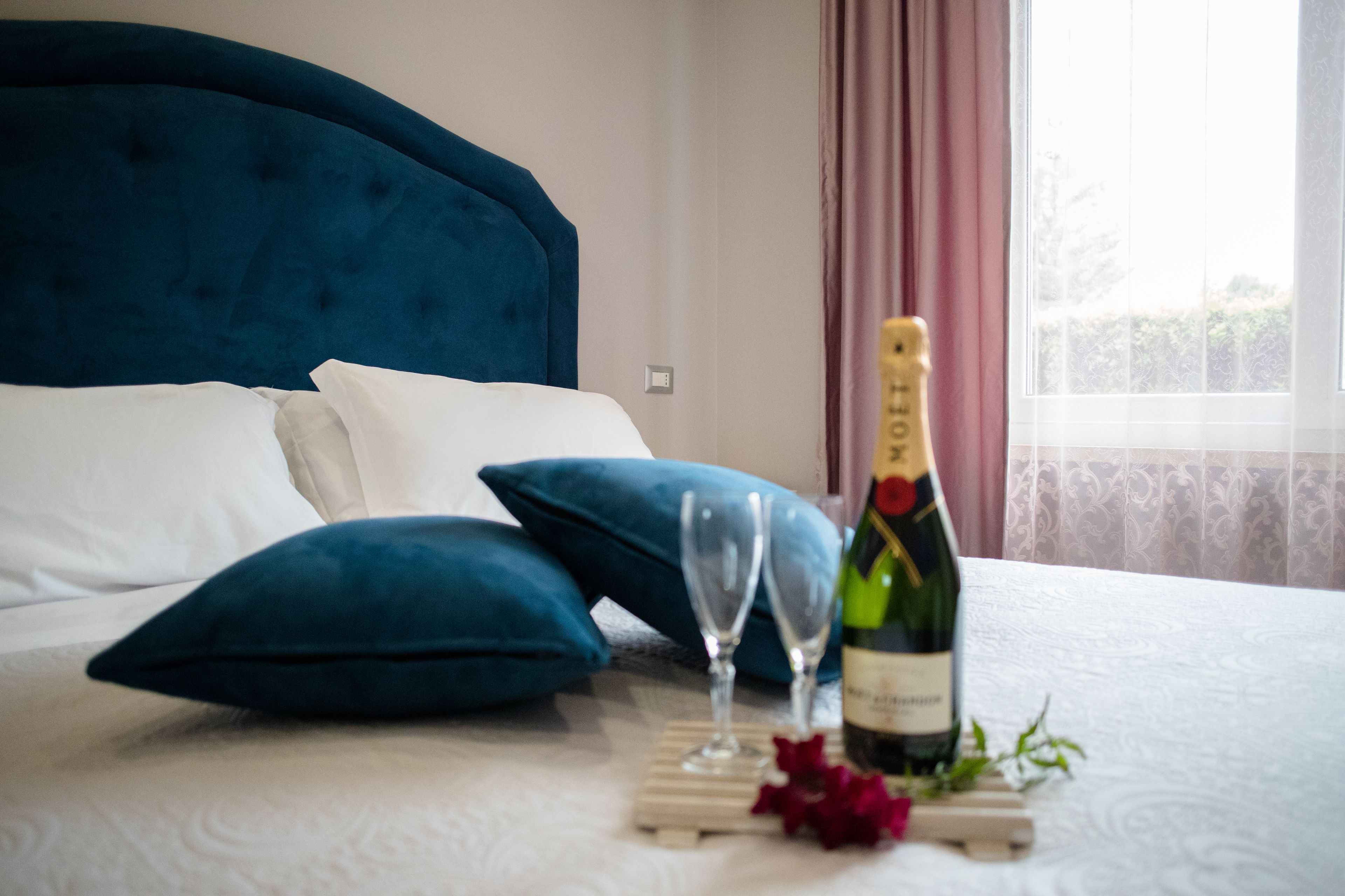 A bed with a dark headboard, white pillows, and a bottle of champagne on a tray with two glasses.