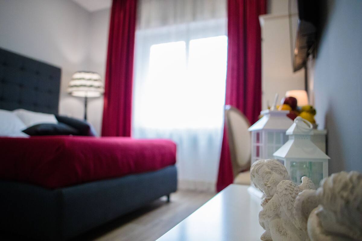A bedroom with a bed, a nightstand, a lamp, and a window with curtains.