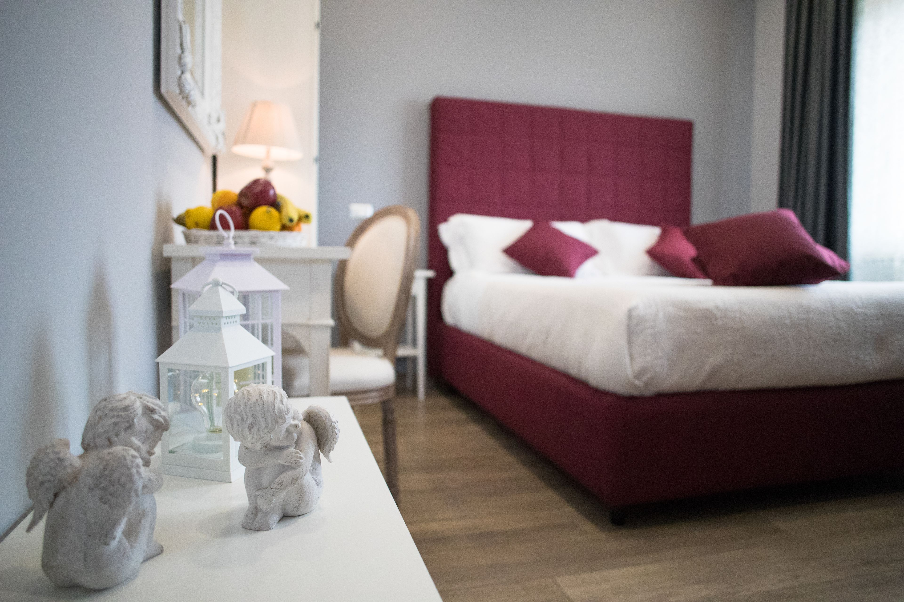A hotel room with a bed, a bedside table with a lamp, a fruit bowl, and two angel figurines.