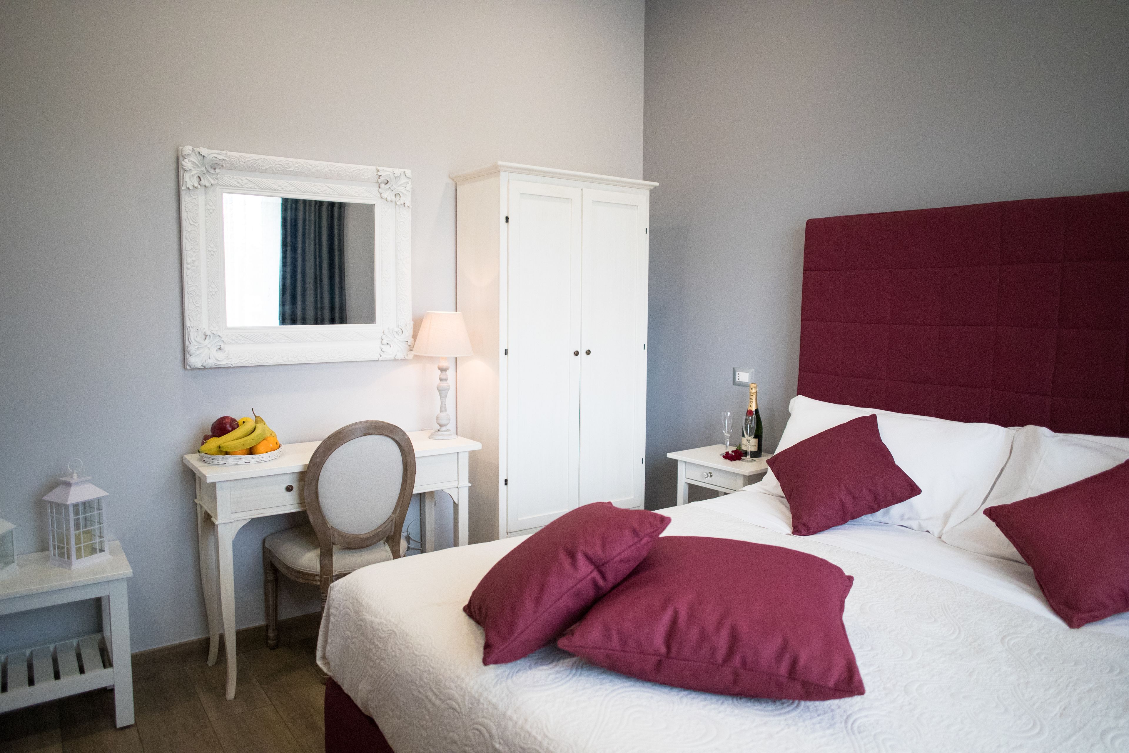 Un dormitorio ordenado con una cama, un escritorio, una silla, un guardarropa y una mesita de noche con una lámpara.