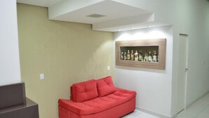 Una habitación con un sofá rojo, una repisa con botellas y una puerta.