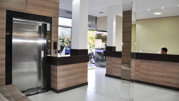 Un área de recepción moderna con un mostrador, un elevador metálico grande y una pared de vidrio.