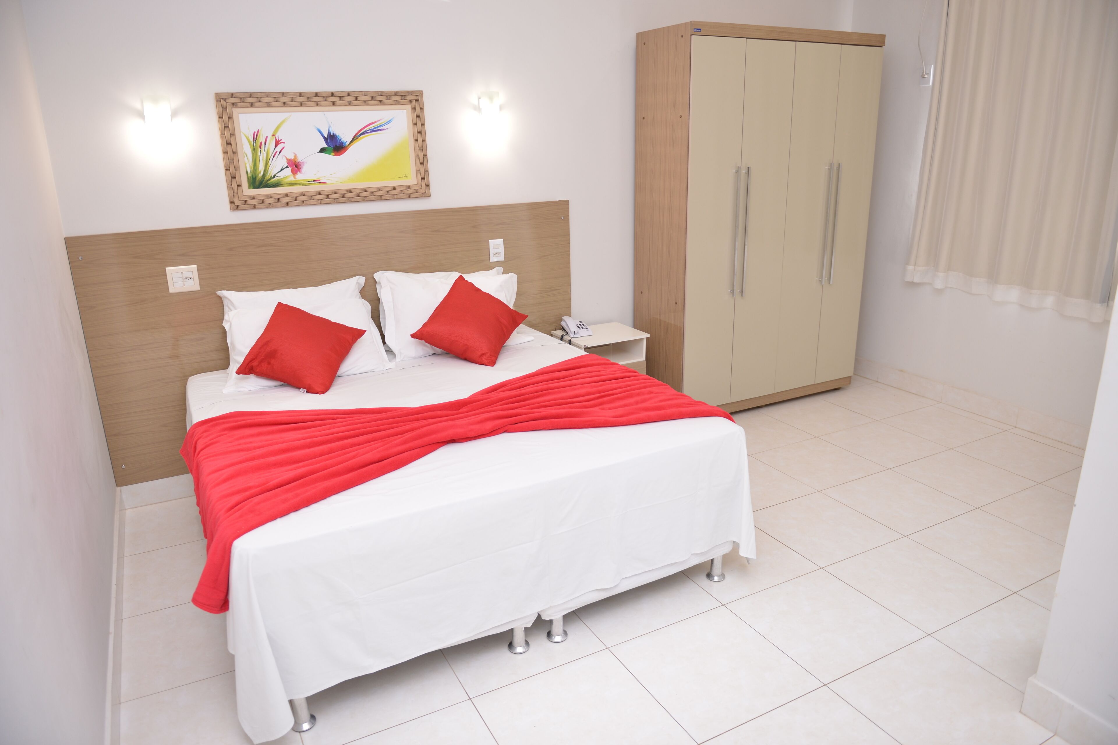 Una cama bien hecha con ropa de cama blanca y roja, un cabecero de madera y una mesita de noche con un teléfono.